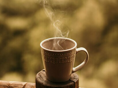 Uma caneca de café recém-preparado repousa sobre uma estrutura de madeira, ainda envolta pelo vapor. No texto, aquele café compartilhado durante a jornada de trabalho se torna símbolo das relações construídas dentro da oficina e das histórias que permanecem mesmo depois de tantos anos