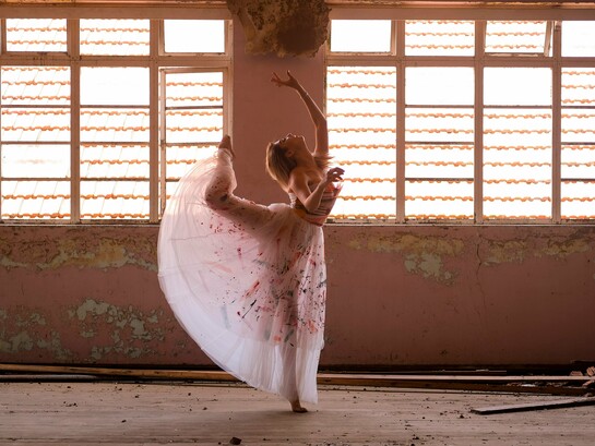 Uma bailarina encontra, entre a luz e as marcas do tempo, a delicadeza de um gesto suspenso. Há movimentos que o corpo aprende, mas há outros que parecem nascer de um fogo interior que o tempo não consegue apagar. Sob a luz que atravessa o antigo espaço, a bailarina transforma o próprio corpo em gesto e presença. Como na vida, a dança não interrompe o tempo: encontra novas formas de continuar