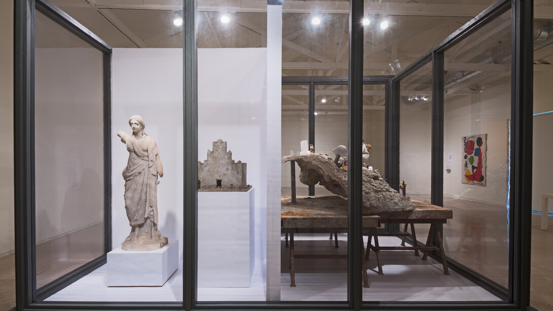 It Takes a Village, (2015), is a new, site-specific work installed in a large glass vitrine and includes various found objects, including Mexican clay figurines, artificial aloes, a plastic radio, a marble statue, Spanish moss, and Mexican colonial painting, among others