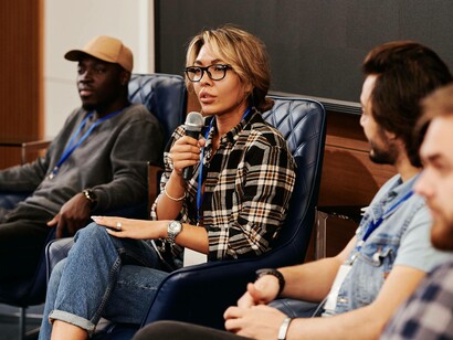A woman is sitting down and holding the microphone while talking to the audience