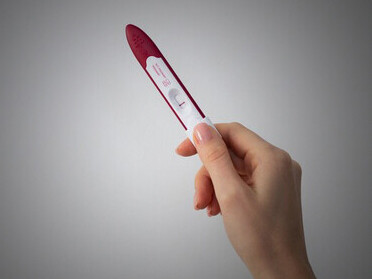 A hand gripping a negative pregnancy test, representing the heartache and struggles associated with infertility