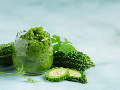 A glass of bitter gourd smoothie topped with chopped bitter gourd