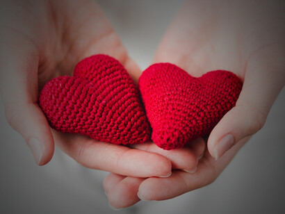 A close-up of hands gently holding a knitted heart, symbolizing warmth and care