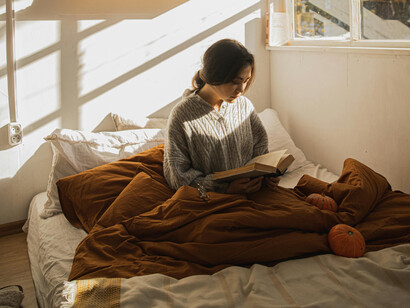A woman reading on her bed as the morning sun lights up her room