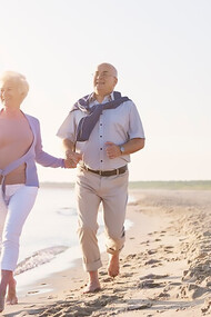 A senior couple enjoys their summer vacation, running along the beach together