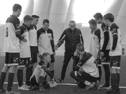 A group of academy players gathered on a well-maintained grass field inside a modern football training complex