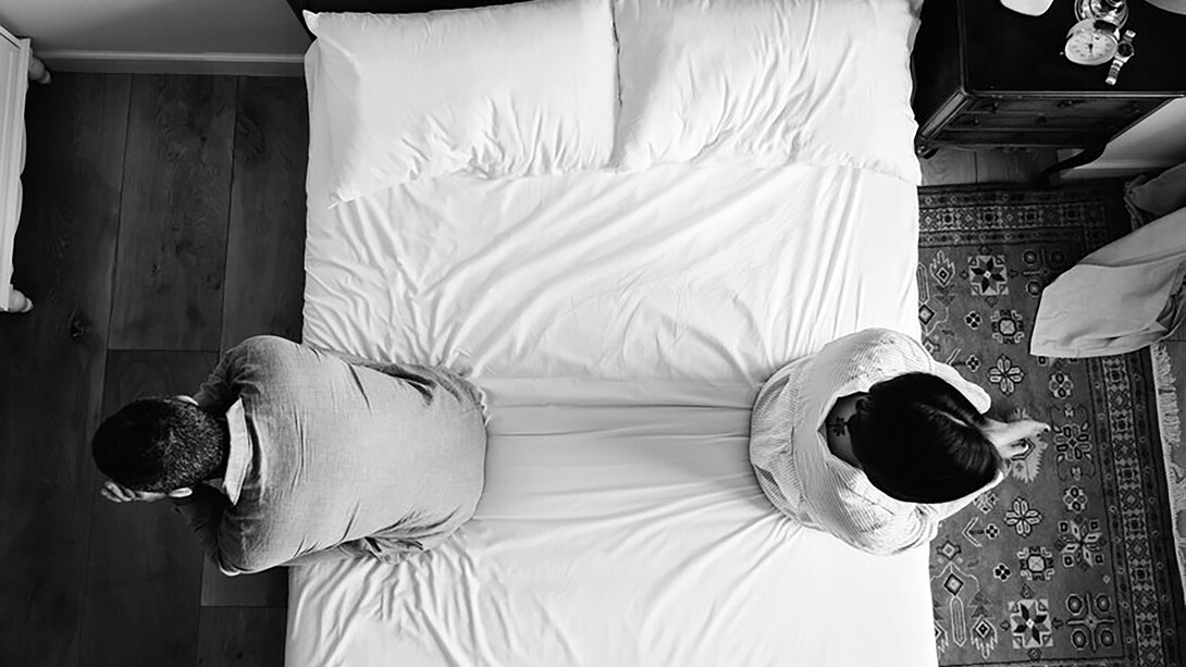 A sad couple sitting back-to-back on the bed, overwhelmed by emotional distress and a broken heart