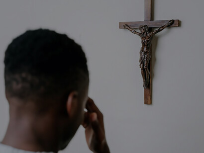A person engages in heartfelt prayer while standing before a wooden crucifix adorning the wall, embodying a moment of profound spiritual contemplation