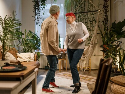 O casal dança alegremente em um ambiente doméstico cercado por plantas, compartilhando um momento de espontaneidade. A vida também pode ser redesenhada quando deixamos de enxergar apenas os caminhos que nos foram apresentados