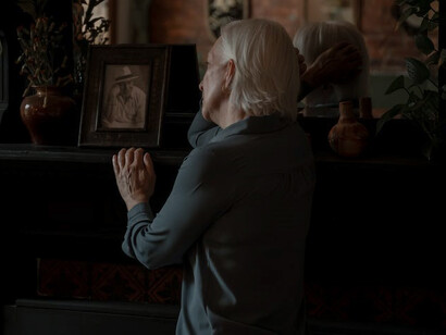 Aged and bereaved, the old woman's eyes fixate on a photograph, her countenance etched with profound sorrow, encapsulating the depth of her grief