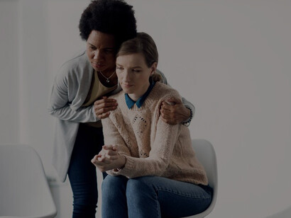 A caring African American woman consoles a sad woman before a group therapy meeting, fostering self-awareness and personal transformation