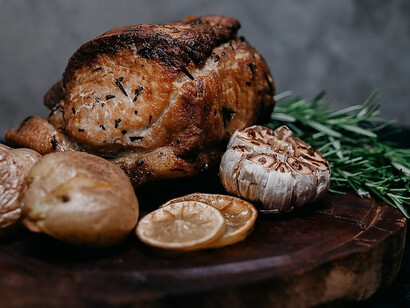 A piece of cooked meat is paired with tender potatoes and accompanied by the zesty brightness of a lemon and garlic, all elegantly presented on a rustic wooden board