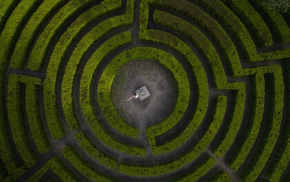 A person standing at the heart of a vast maze, symbolizing humanity’s struggle to maintain direction during times of uncertainty