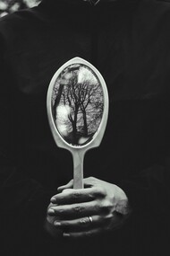 A person holding a hand mirror toward the autumn forest, reflecting shifting perspectives
