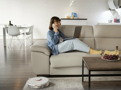 A homeowner seated comfortably while a robotic vacuum operates nearby, illustrating the seamless integration of technology into daily life