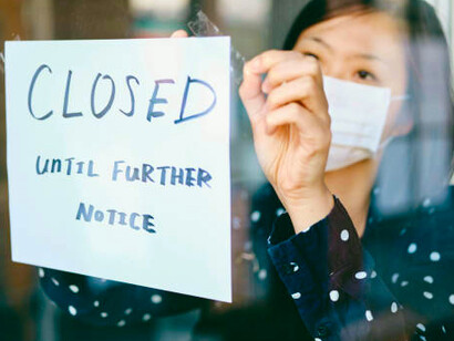 A small business owner affected by COVID-19 holds a sign that reads, "Closed until further notice"