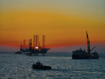 Offshore oil platforms against the setting sun, representing the fossil fuel industry at the center of the climate liability debate