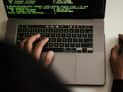 An unrecognizable developer using a laptop and smartphone beside a high-end custom-built PC