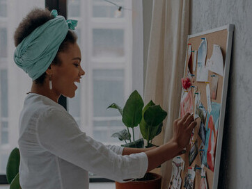 A woman in a white long-sleeve shirt placing a pin on her vision board, symbolizing goal setting, priorities, and the discipline needed for success