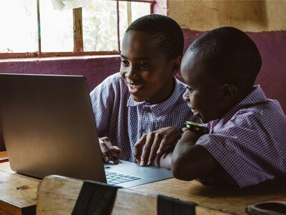 Schoolchildren gathered around a glowing laptop in a modest classroom, representing the expanding reach of digital education across East Africa