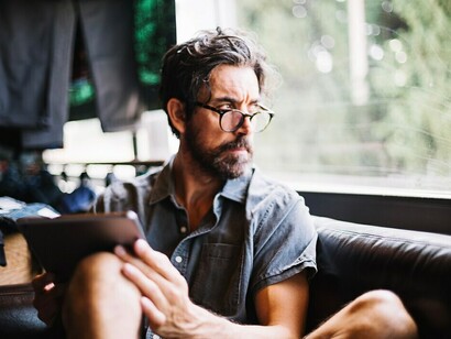 A man using a tablet while looking out the window, working as a freelancer with a flexible routine