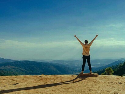 A hiker reaching the top of a summit and raising their arms in victory by doing their part to improve the climate
