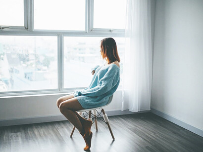 A woman gracefully seated on a sleek black chair, positioned before a glass-paneled window adorned with flowing white curtains
