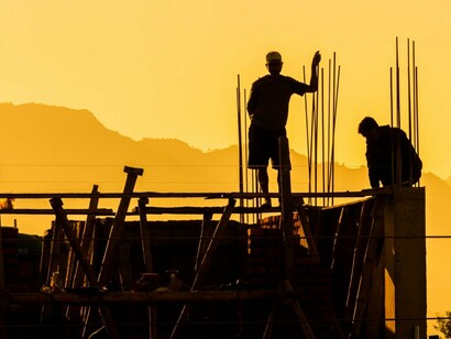Silhouettes of laborers reinforcing a building frame, reflecting the often-unseen work behind progress