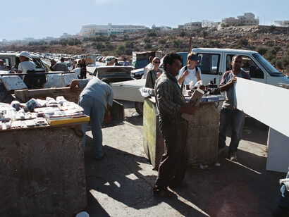 Des Palestiniens transbordent des matériaux de construction d’un camion à un autre afin de franchir un barrage routier israélien non gardé entre deux villes palestiniennes de Cisjordanie occupée, août 2004