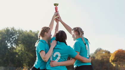 Girls celebrating with raised trophies at an awards ceremony, showcasing community recognition and public appreciation events