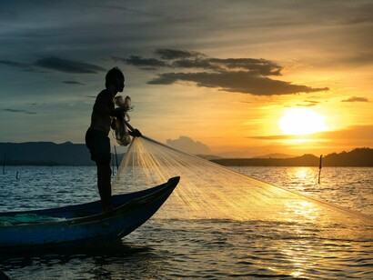 A lone fisherman casting his net across the waters at sunset, representing the quiet burdens Vương carried after setting aside his dreams for his family