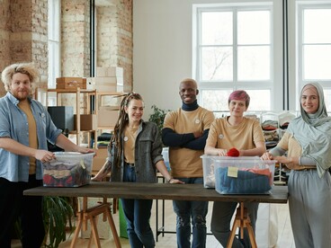 Equipe de voluntários reúne-se diante de caixas com roupas destinadas à doação. A articulação entre pessoas, recursos e processos é fundamental para organizações que buscam ampliar sua atuação e gerar impacto em maior escala