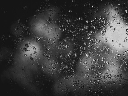 Raindrops blur the world outside, reflecting the quiet exile within