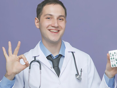 Young male doctor, adorned in medical attire with stethoscope around his neck, smiles as he holds medication in hand