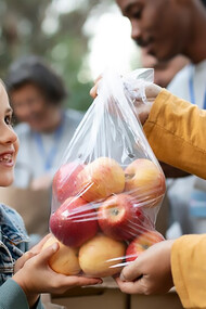 A child holding a bag of apples, offering it as a donation