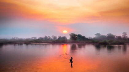 A man fishing on the Mekong River in Laos as the sun sets
