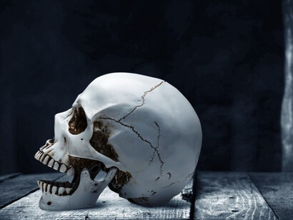 A human skull placed on a wooden table, set against a shadowy backdrop