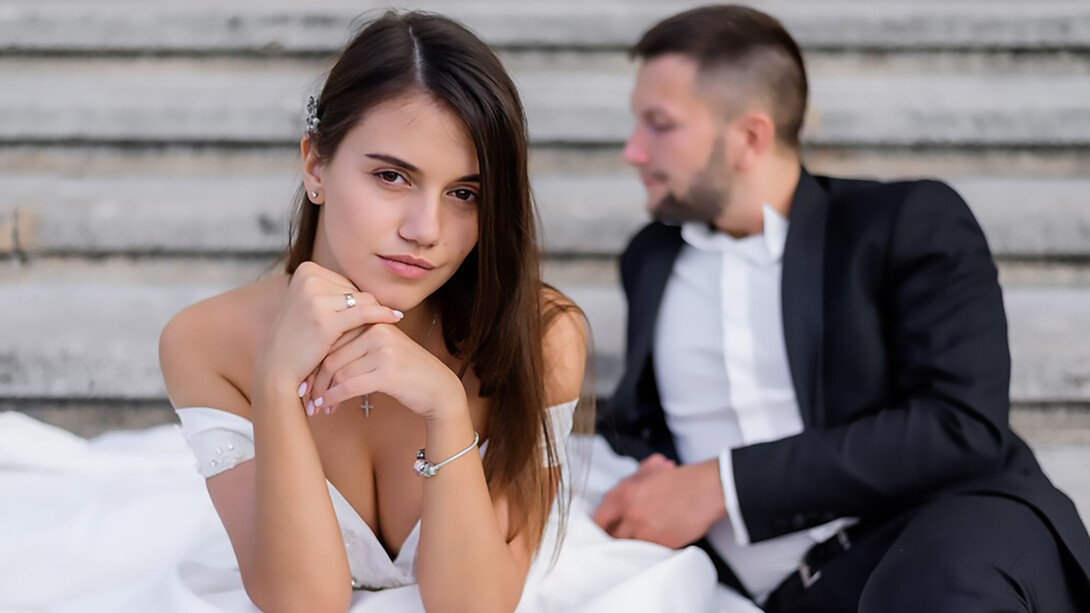 Brunette bride gazing confidently at the camera with the groom seated in the background