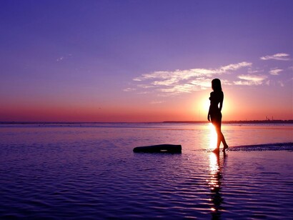 Una mujer camina por la orilla del mar al atardecer