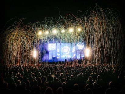 The lights continue to shower down on the audience as the performers take the stage
