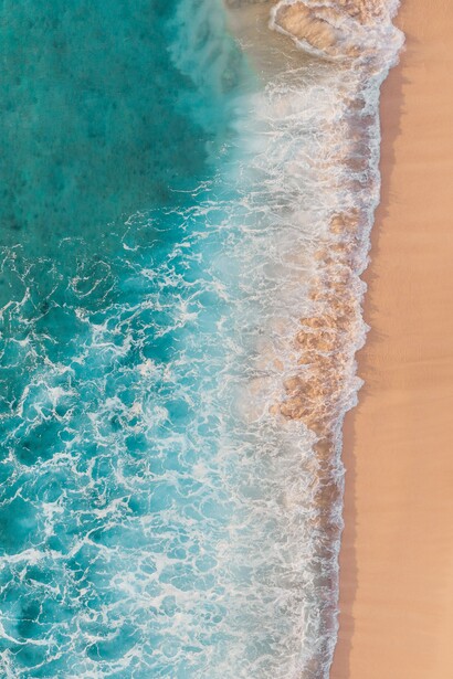 As ondas avançam sobre a areia em uma faixa contínua de espuma, vista de cima. O movimento permanente da água dialoga com a ideia de transformação e com a necessidade de abandonar padrões que já não fazem sentido