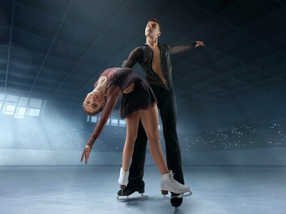 A figure skating couple performs gracefully in a cold, empty ice arena, illuminated by a spotlight on the rink