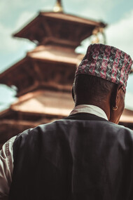 A Nepali man stands in the foreground, gazing at the majestic temple in Patan, Nepal, surrounded by the rich cultural architecture of the ancient city