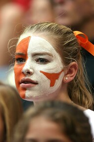 Blonde woman with orange and white face paint watching a football match