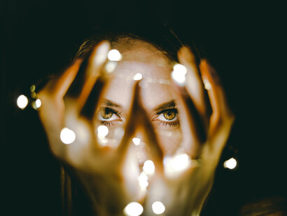 Mujer observa sus manos cubiertas de luces con una mirada desafiante. Todo es transmisible, fusionable, enmudecedor y creador