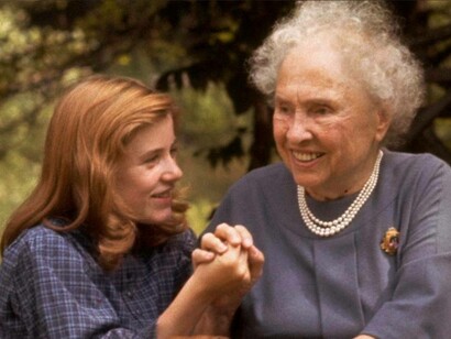 An older Helen Keller being helped by one of her relatives through the park