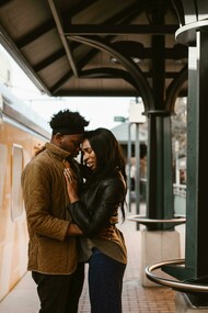 A couple hugs beside an orange train, sharing an emotional moment in a long-distance relationship