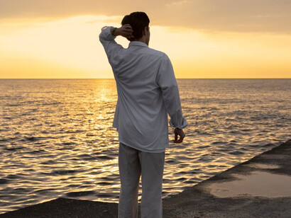 A man standing by the sea, deep in thought, as if breaking free from the weight of his past