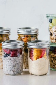 Six fruit cereal portions stored in glass mason jars, set on a white surface for easy meal prep