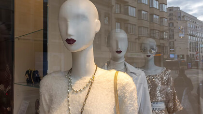 A white human skull wearing a yellow shirt displayed in the window of a luxury fashion store.